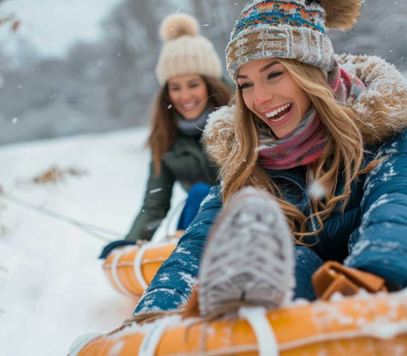Joyful women brave the freezing winter weather, bundled up in warm clothing and sporting bright smiles as they ride their sleds down a snowy hill with a child, making memories in the great outdoors